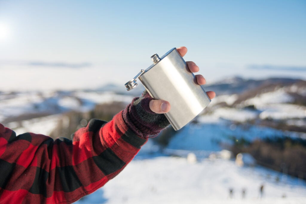 Male hand holding hip flask on a snowy mountain top