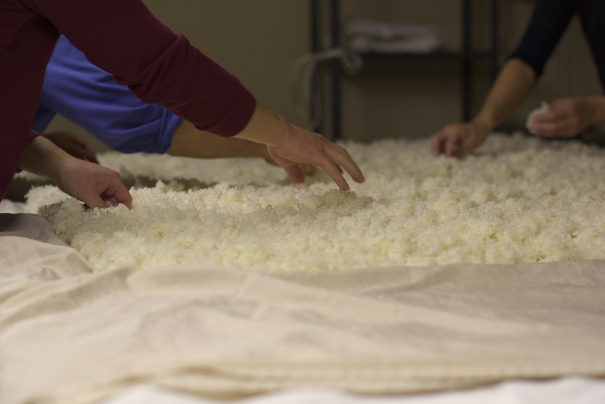 A table spread with cooked rice, people's hands are in shot and moving the rice
