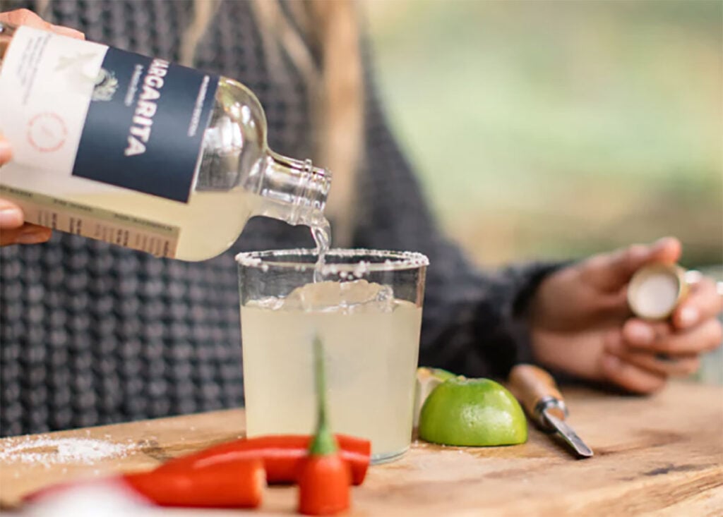 A bottle of Pentire Margarita being poured into a glass with garnishes