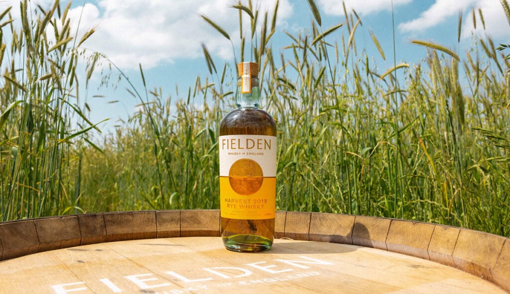 A bottle of Fielden Harvest 2019 Rye Whisky in a field of barley