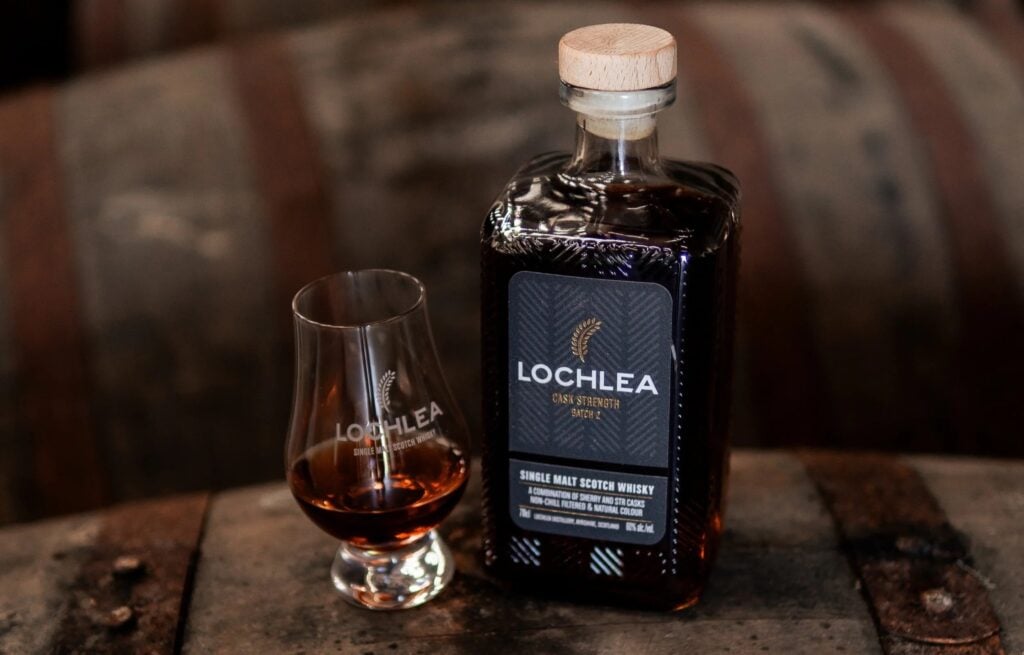 A bottle and glass of Lochlea Cask Strength - Batch 2 on top of a whisky cask