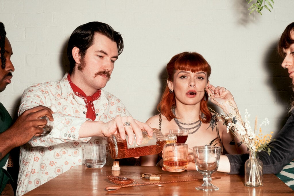 Young people drinking Ninefold rum on a table with glassses, bottles, and bartending equipment.