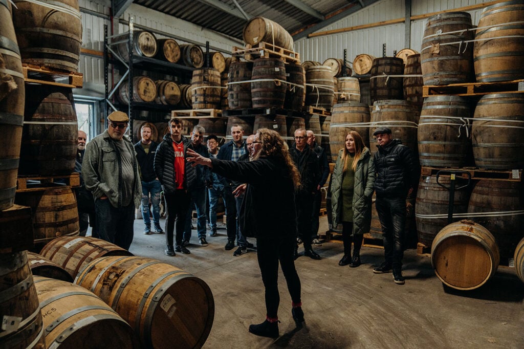 A tour group sees a warehouse at The Cotswolds Distillery