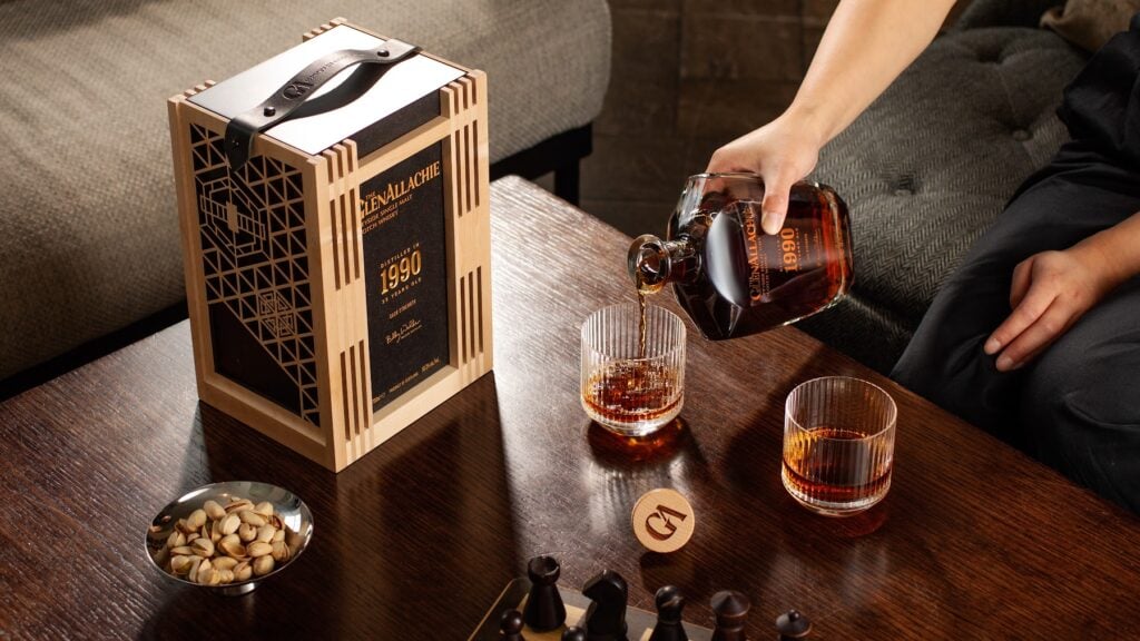 A bottle of The GlenAllachie 35 Year Old Cask Strength being poured into Glencairn glasses on a wooden table with a presentation box
