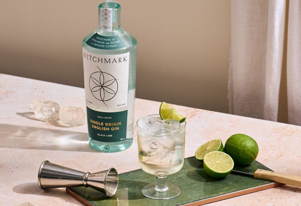 A bottle of Witchmark Single Origin Black Lime Gin with a cocktail