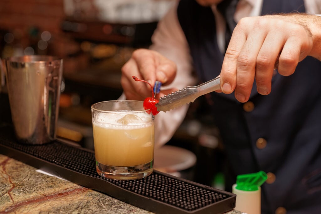 Bartender decorating a Whisky Sour cocktail with cherry