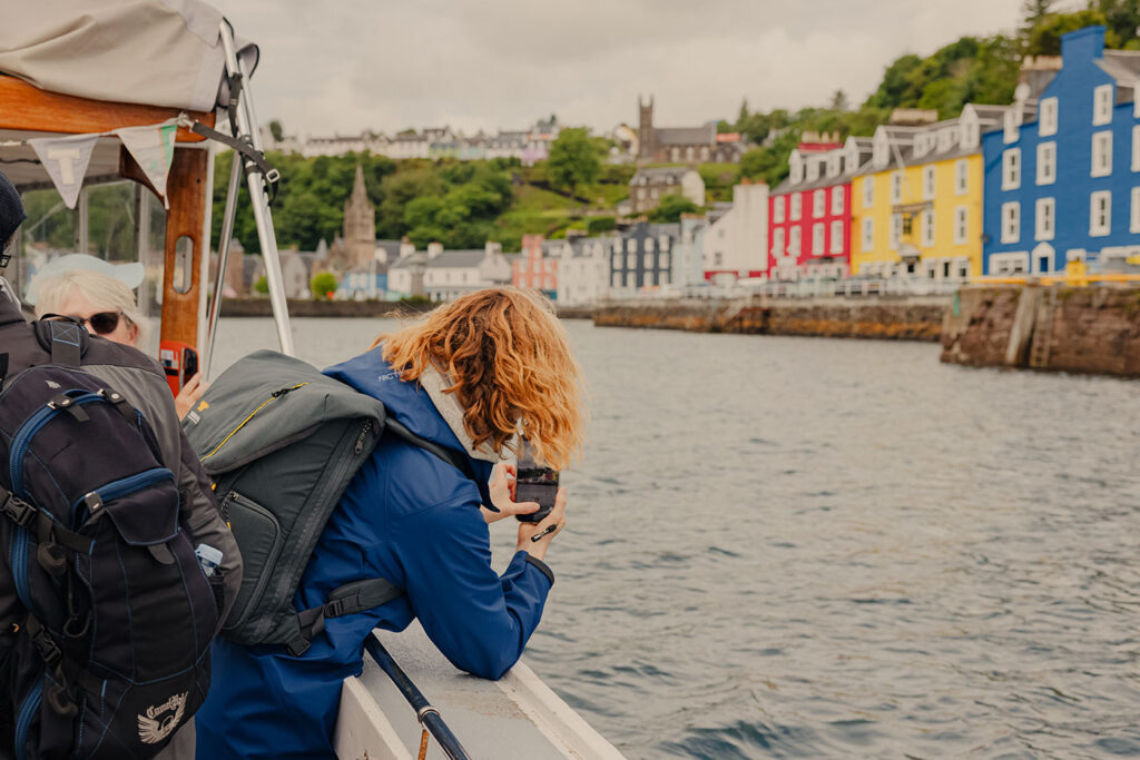 A woman takes a photo of the Isle of Mull from a boat