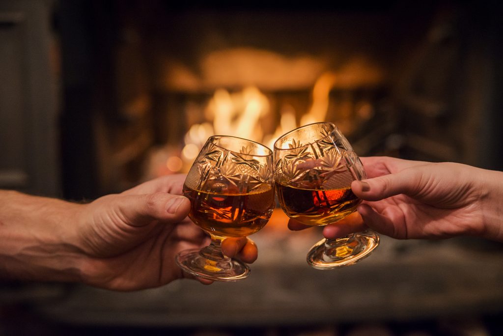 Hands toasting with whiskey in front of fireplace