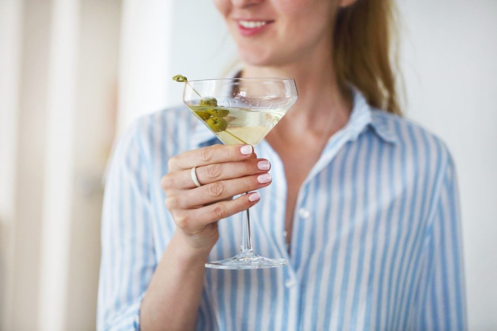 Woman holding glass with martini and green olives, easy cocktails to make at home