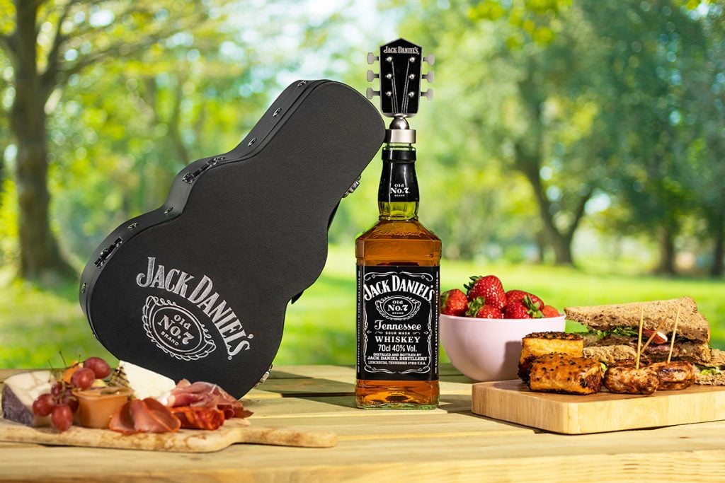 The Jack Daniel's Guitar Case Gift Pack surrounded by food on a wooden table in a field