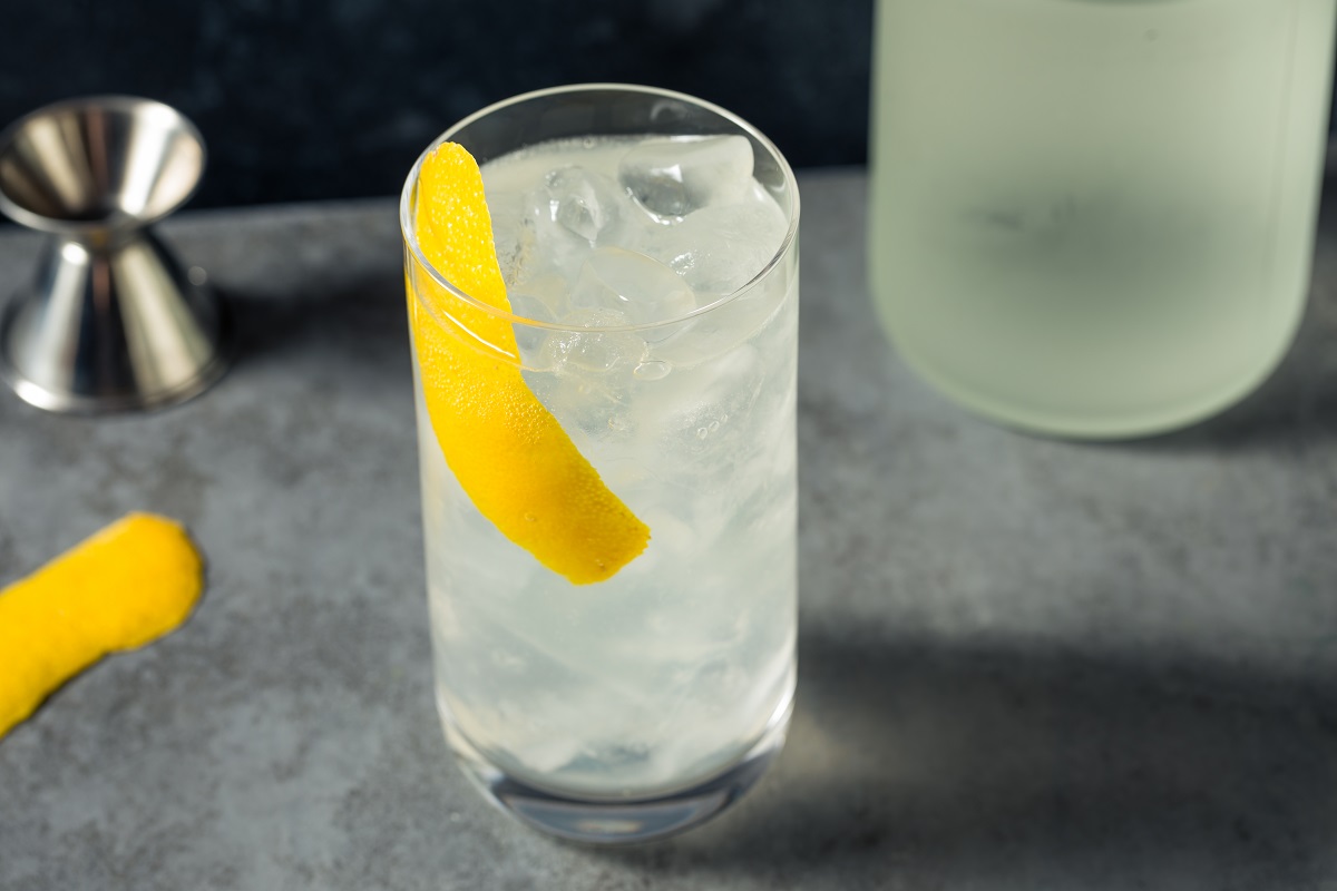 A table with a tall glass filled with ice and cloudy liquid, with a strip of lemon zest as a garnish