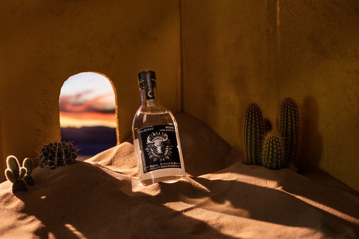 A bottle of Tres Tribus Mezcal in a room filled with sand and cacti
