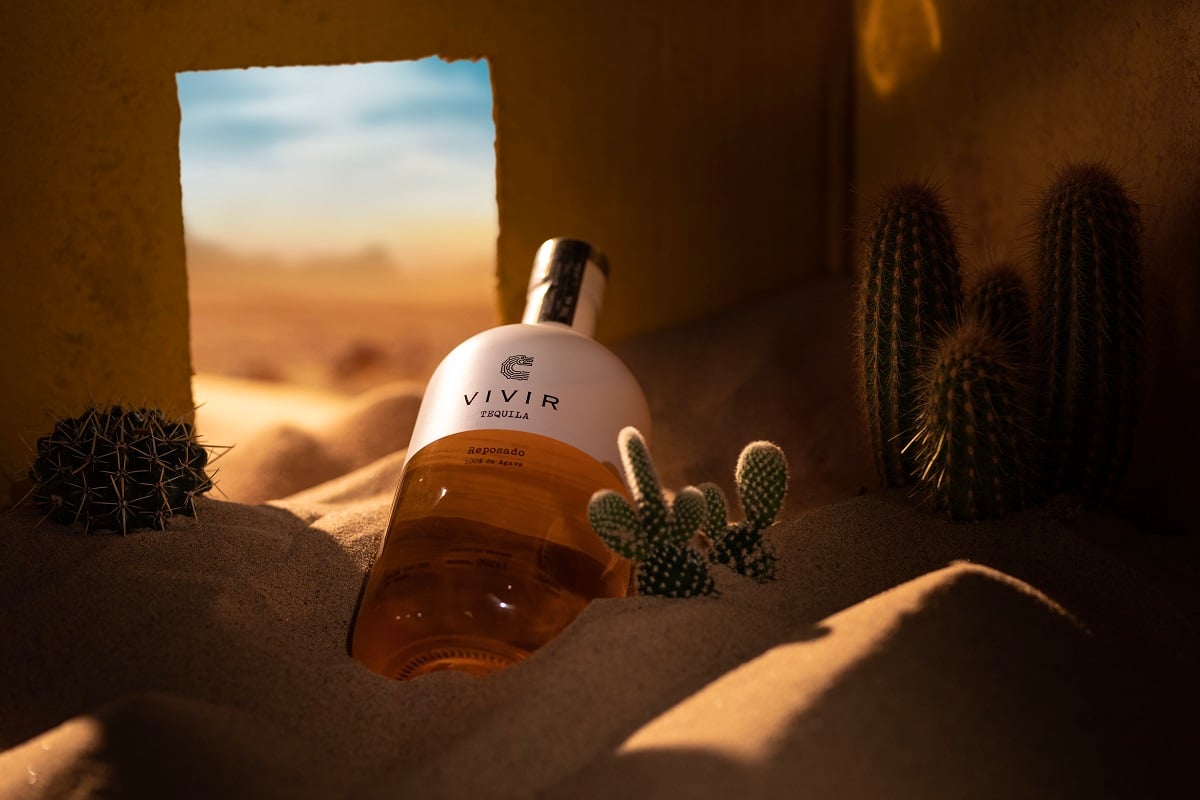 A bottle of VIVIR Tequila Reposado in a room filled with sand and cacti