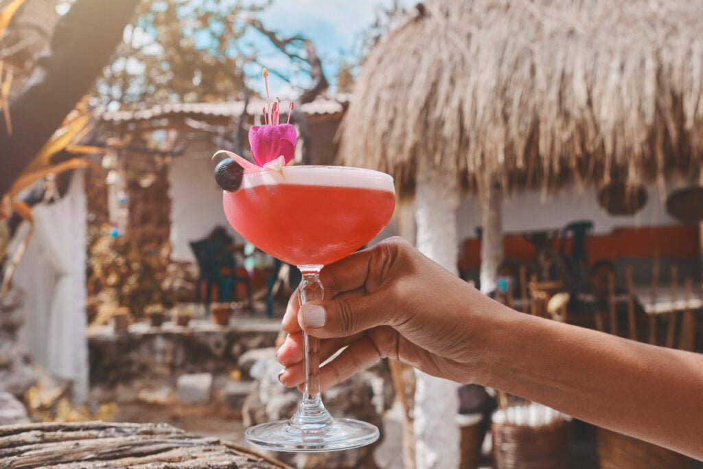 A person is holding a glass of pink drink with a flower on top