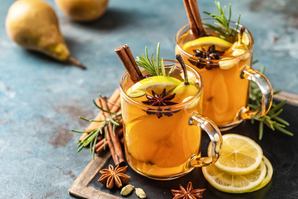 Hot drink cocktail for New Year, Christmas, winter or autumn holidays. Toddy. Mulled pear cider or spiced tea or grog with lemon, pear, cinnamon, anise, cardamom, rosemary.
