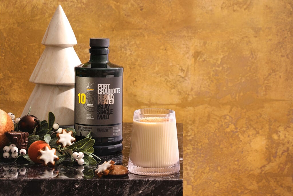 A bottle of Port Charlotte 10 Year Old surrounded by Christmas decorations and an eggnog. The Best Whisky Eggnog, according to Master of Malt in 2025.