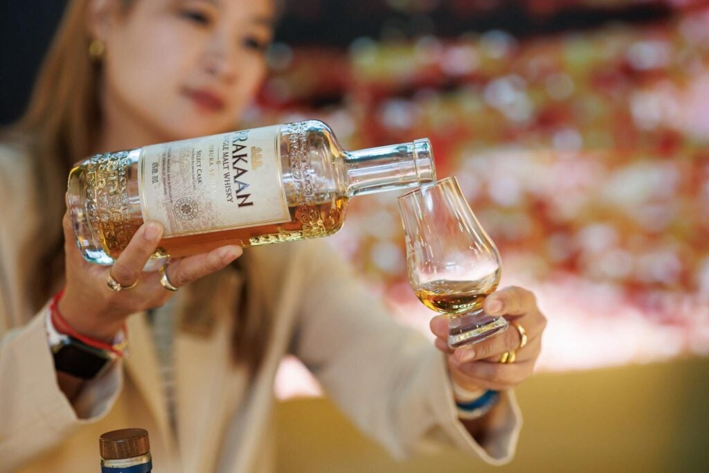 A Thai lady pouring Prakaan Whisky into a Glencairn Glass.