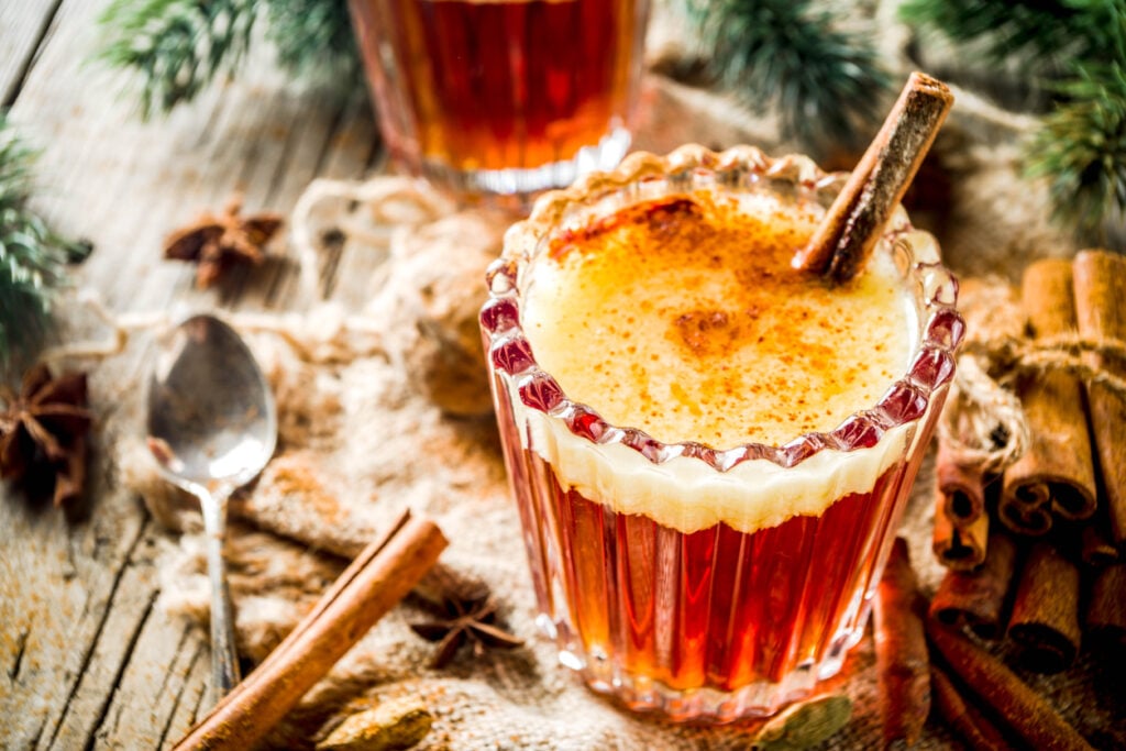 Winter holidays traditional drink, homemade hot buttered rum with spices, over old rustic wooden background with christmas tree branches, copy space