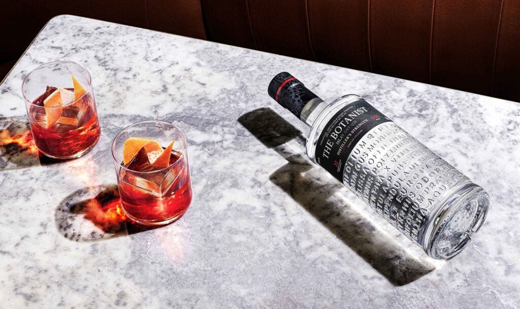 The Botanist Distiller's Strength on a marble table with two Negronis close by